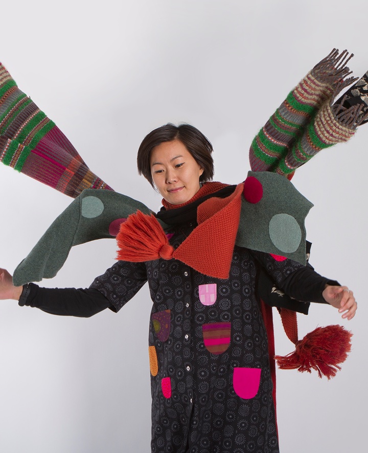 Sieun wearing a colourful handmade knitted costume with wing-like arm extensions